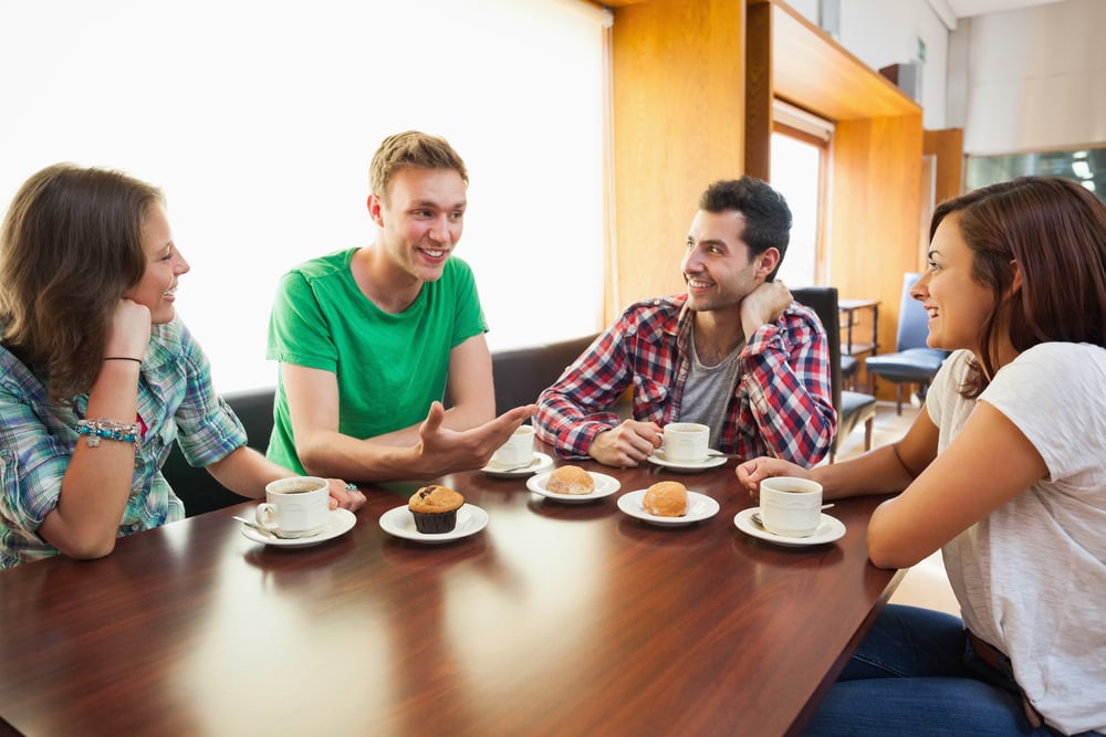 Four casual students having a cup of coffee chatting in college canteen